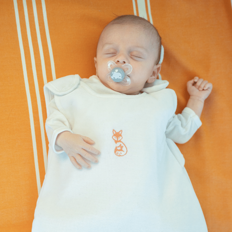 Gigoteuse hiver naissance blanche sans manche portée par un bébé qui dort de face Gigoteuse hiver naissance blanche sans manche portée par un bébé qui dort de face